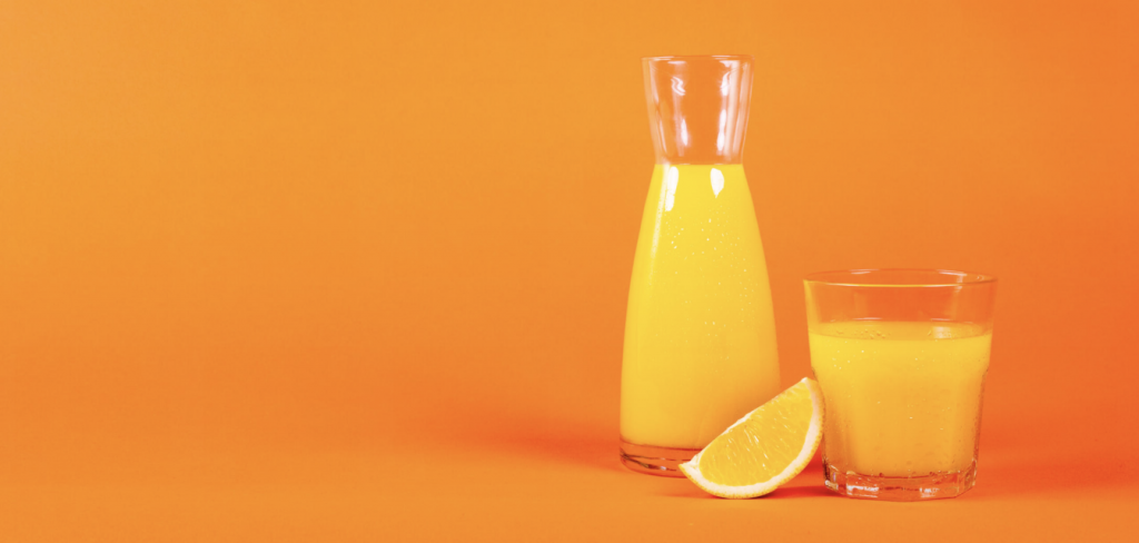 carafe of orange juice, a cup of orange juice and a slice of an orange