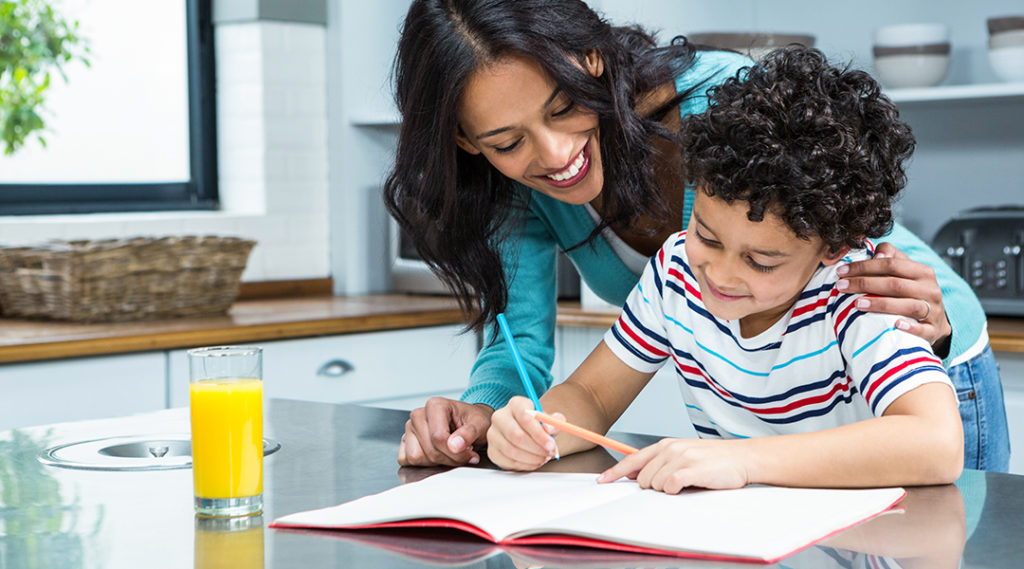 adult woman helping child with homework at table with glass of orange juice