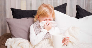 sick child blowing nose with a cup of tea