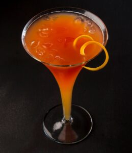Red/Orange colored cocktail in glass with orange zest twist.