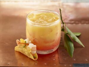 A Tequila Sunrise Cocktail with a ceviche taco next to it.