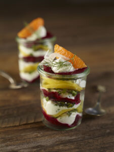 Mason jar with layered potatoes, dyed from beets. Topped with orange slice and greens.