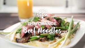 Plated noodles topped with greens and sliced beef.