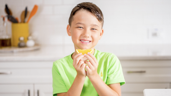 young boy smiling while holding an orange slice