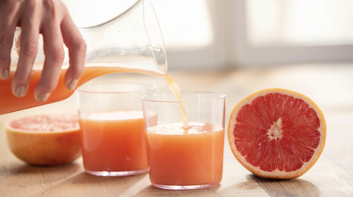 carafe with grapefruit juice being poured into a glass next to a slice of grapefruit