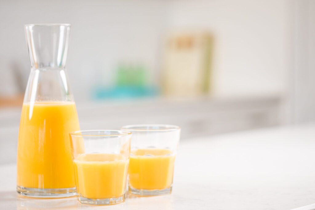 Two small glasses of orange juice with a full carafe